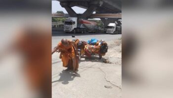 Монах-самозванец тащит мотоцикл по дороге в Корат