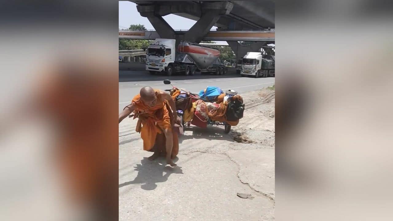 Монах-самозванец тащит мотоцикл по дороге в Корат