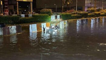 Подросток, получивший удар током, толкает мотоцикл по затопленной дороге